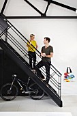Woman and man on black metal staircase with bicycle stored below in loft apartment