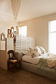 Romantic bedroom with pale green cushion platform bed and artistic white screen against partition separating ensuite bathroom with gallery of nostalgic mirrors