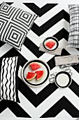 Cushions with graphic, black and white patterns and plate of red melon slices against bold, zigzag background