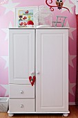 White wardrobe with heart-shaped pendant against pink-painted wall with pattern of stars