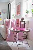 Rosefarbene Sektkelche und Windlicht auf Tabletttisch neben Sofa mit pastellrosa Kuscheldecke