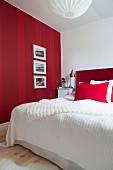 Framed pictures on red striped wall next to bed with red headboard