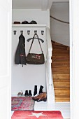 Garderobenhaken, Hutbord und Schuhe am Boden neben einem Treppenaufgang in weisser Diele mit roten Teppichen