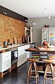 Kitchen unit in front of brick wall and kitchen island with storage space for books and vintage bar stools