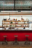 Bar in former workshop with red bar counter, vintage swivel stools and long shelves of bottles