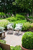 Wooden folding chairs with cushions on terrace in garden with pink and white lupins and sculptures of birds