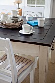 Coffee service on rustic dining table with dark wooden top and white wooden chairs with seat cushions