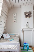 Child's attic bedroom with white wood cladding and blue stool next to bed
