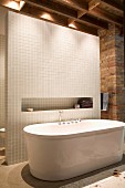 Freistehende Designer-Badewanne vor gefliestem Raumteiler mit schmaler Öffnung in rustikalem Ambiente