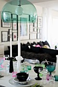 Various goblets and glasses of different colours on table below pendant lamp with green transparent lampshade