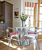 Classic, metal chairs and round table in front of open terrace door with red and white striped Roman blinds on windows