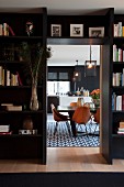 Black fitted shelving as partition with open doorway and view of elegant dining area with retro, wooden shell chairs