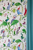 Ausschnitt einer Tapete mit Karikatur Papageien- und Blättermotiven, seitlich pastellblauer Vorhang