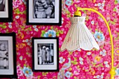 Standard lamp with nostalgic lampshade in front of framed black and white photos on floral wallpaper