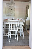 Set table and white wooden chairs in rustic dining room seen through open door