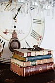 Stack of antiquarian books and bunch of keys on surface in front of old clock face