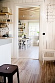 Rustic kitchen with retro stool on wooden floor and view into dining room through open door in background