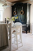 Corner of dining set with white kitchen chairs in front of black farmhouse cupboard decorated with wreaths