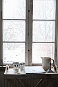 Jug and glasses on tray table below window with view into snowy garden