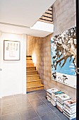 Treppenaufgang und Galeriebrüstung in offener Diele; Zeitschriftenstapel und Bild auf grau verputzter Wand