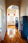 Hallway with arch, white wood-clad walls, blue vintage metal cabinets and rustic wooden floor