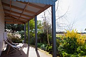 Holzliegestühle auf überdachter Terrasse, weiter Blick über sommerlichen Garten in die Landschaft