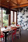 Red and white chairs at rustic wooden table in front of wall covered in floral wallpaper