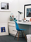 Collection of modern artworks in study with white fitted desk, blue Eames Chair and table lamp by Louis Poulsen