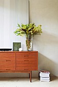 Objets d'art and vase of flowers on sixties sideboard next to stack of magazines