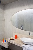 Waschtisch mit weisser Porzellanschüssel auf abgetreppter Betonablage und ovaler Spiegel an Betonwand