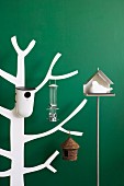 Various bird feeders and nesting boxes hung on white. stylised wooden tree against wooden wall