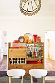 Chair backs in front of small home bar with red ornaments; views of kitchen counter and coat stand through open doors in background