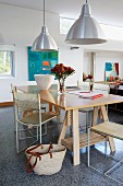 Simple table top on wooden trestles and delicate metal chairs below retro metal pendant lamps in modern interior with terrazzo floor