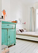 Shabby-chic bedroom with turquoise baby-changing cabinet, white-painted wooden floor and curtains made from bed linen