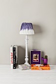 Table lamp with dip-dyed lampshade next to books on pale surface against pale grey wall