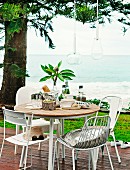Various metal chairs around round table on wooden deck with sea in background
