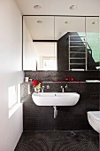 Weisses Waschbecken an Wand mit schwarzen Mosaikfliesen unter Spiegelschrank