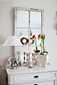 Table lamp with white lampshade and potted plant in front of wood-framed, lattice mirror on rustic chest of drawers