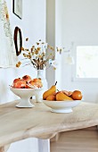 White ceramic bowls of fruit and vase of dried flowers on wooden surface