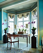 Purple potted orchids flanking workspace with antique writing desk and chair in window bay of grand salon with walls painted light blue