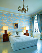 Double bed with white, tailored bed cover flanked by table lamps on Biedermeier-style bedside cabinets in grand bedroom