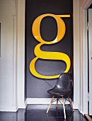 Charles Eames shell chair below huge decorative letter G on dark-painted wall