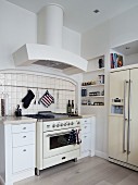 Vintage kitchen cooker flanked by modern, country-house-style, white cabinets with drawers below extractor hood in corner of kitchen