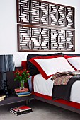 Double bed with red and white bed linen below antique wooden lattice panels mounted on wall