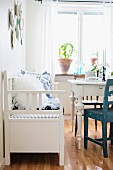 Rustic, white bench and table in front of potted plant on windowsill in simple dining room