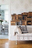 Vintage couch with white metal frame and lacy throw in front of stacked, antiquarian books on sideboard; view into dining room through open doorway to one side