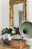 Vintage gramophone on console table below gilt-framed mirror on wall