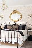 Vintage Einzelbetten aus schmiedeeisernem Gestell nebeneinander gestellt vor tapezierter Wand mit antikem, ovalem Spiegel in Goldrahmen
