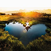 Woman meditating next to heart-shaped mountain pond