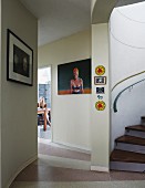 Artworks on painted foyer wall, foot of spiral staircase and view of young woman through open door in background